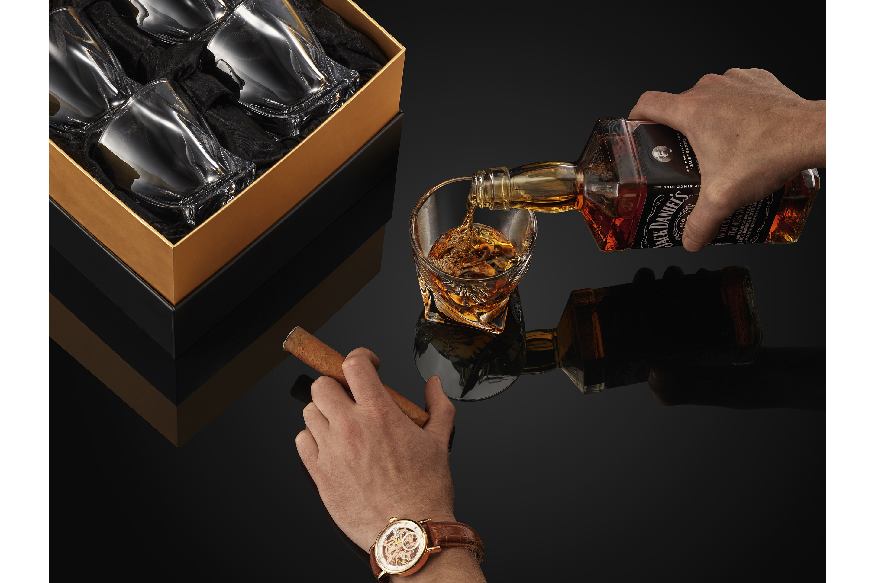 Person pouring whisky into glass on a back backdrop with whisky glass in packaging photo shoot